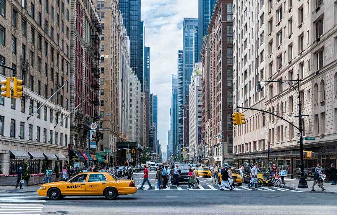 En typisk gata i New York med skyskrapor på båda sidorna, gula taxibilar och folk som går över ett övergångsställe.